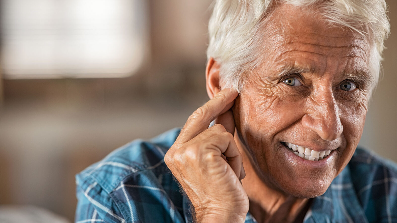 smiling older white man touching his finger to his ear trying to listen