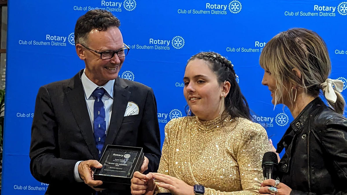 Sham receiving her shine award from Rotary representatives on a blue rotary stage